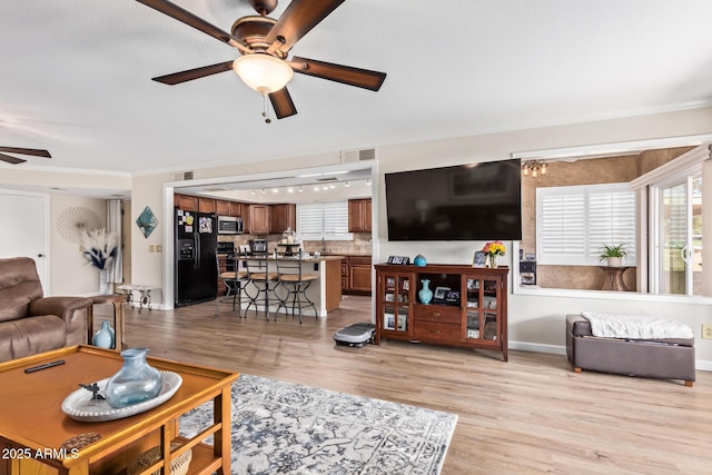 living room featuring light wood-style floors, visible vents, crown molding, and a ceiling fan