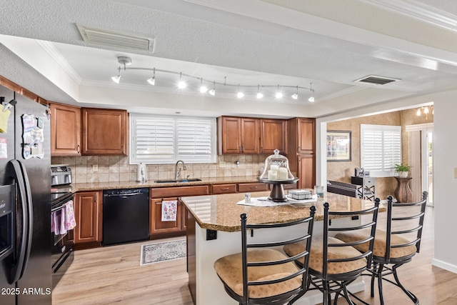 kitchen with visible vents, brown cabinets, a center island, black appliances, and a sink