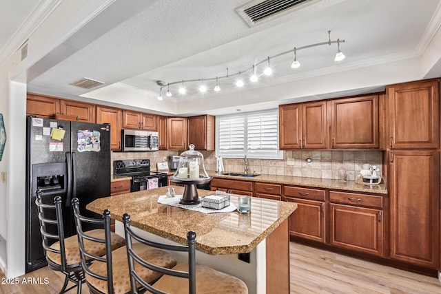 kitchen with visible vents, a sink, a kitchen island, black appliances, and a kitchen bar