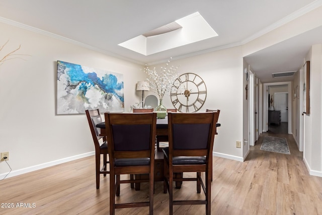 dining space with a skylight, crown molding, light wood finished floors, visible vents, and baseboards