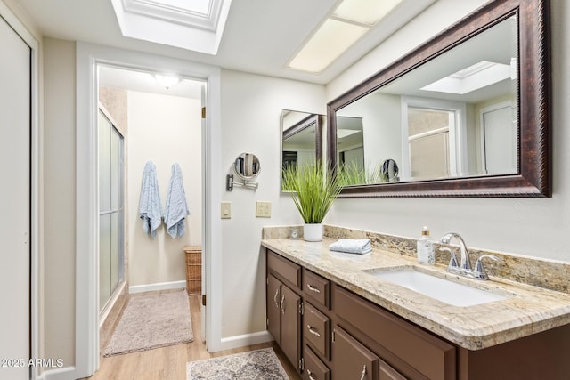 full bath featuring a skylight, vanity, a shower stall, wood finished floors, and baseboards