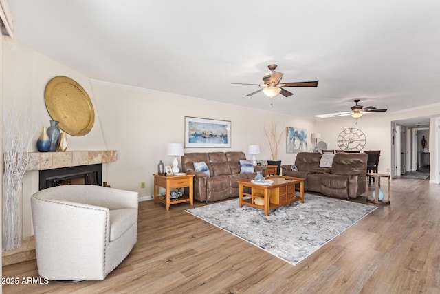 living area with a tile fireplace, ceiling fan, baseboards, and wood finished floors