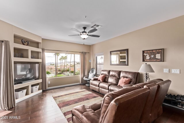 living area featuring built in features, wood finished floors, baseboards, visible vents, and ceiling fan