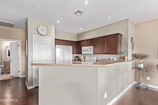 kitchen featuring visible vents, light countertops, a peninsula, dark wood-style floors, and white appliances