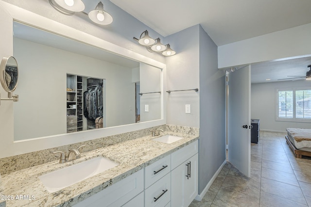 ensuite bathroom featuring baseboards, a ceiling fan, double vanity, and a sink