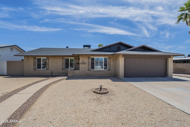 ranch-style house with concrete driveway, roof with shingles, fence, brick siding, and a garage