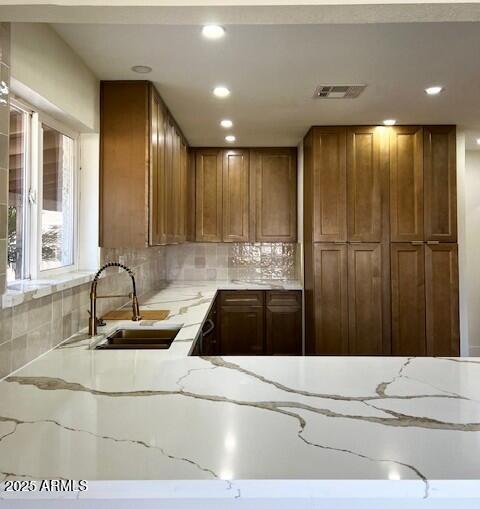 kitchen with brown cabinets, light stone counters, visible vents, and a sink