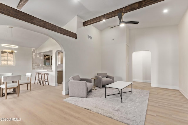 living area featuring visible vents, vaulted ceiling with beams, baseboards, light wood-type flooring, and arched walkways