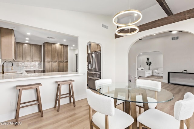 dining area with light wood-style floors, visible vents, and arched walkways