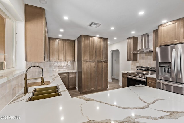 kitchen with visible vents, appliances with stainless steel finishes, arched walkways, wall chimney exhaust hood, and a sink