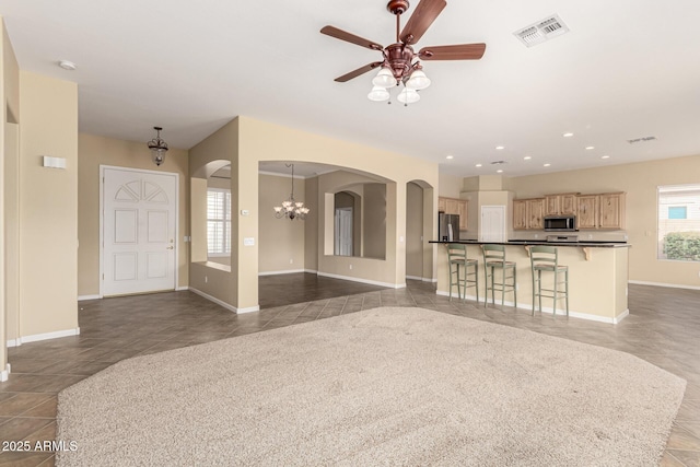 unfurnished living room featuring arched walkways, recessed lighting, ceiling fan with notable chandelier, visible vents, and tile patterned floors