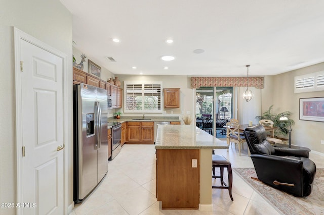 kitchen with appliances with stainless steel finishes, a breakfast bar, sink, hanging light fixtures, and light stone countertops