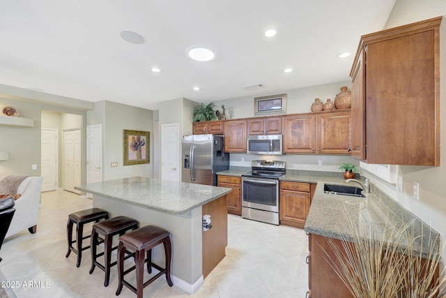 kitchen with appliances with stainless steel finishes, a breakfast bar, sink, a center island, and light stone countertops