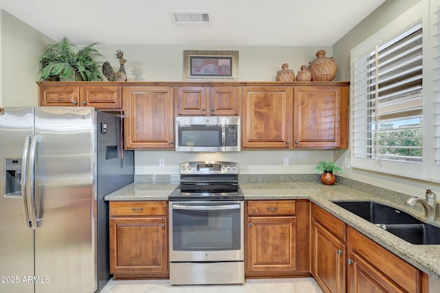 kitchen with light stone countertops, light tile patterned floors, stainless steel appliances, and sink