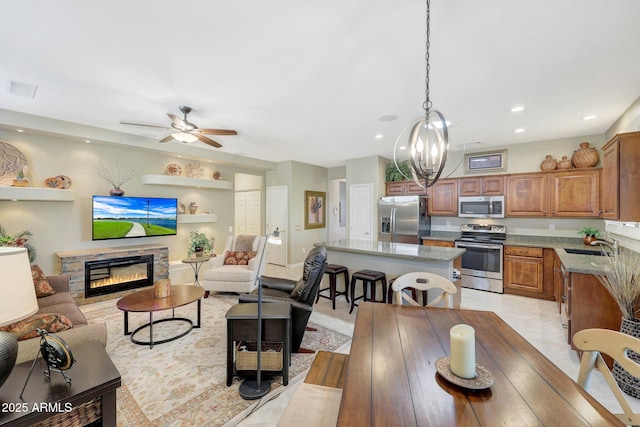 interior space featuring a stone fireplace, sink, light tile patterned floors, and ceiling fan