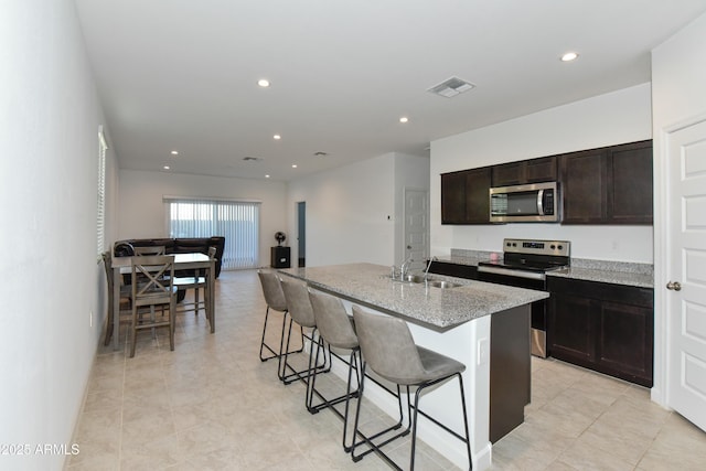 kitchen featuring a kitchen bar, sink, an island with sink, light stone counters, and stainless steel appliances