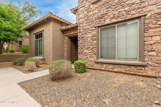 entrance to property featuring stone siding, fence, and stucco siding