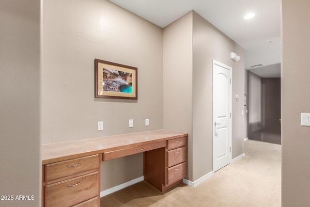 unfurnished office featuring built in desk, light colored carpet, and baseboards