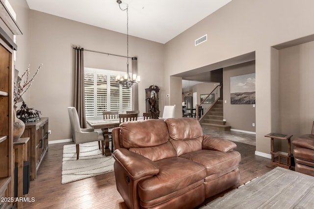 living area with a chandelier, dark wood finished floors, baseboards, stairway, and a high ceiling