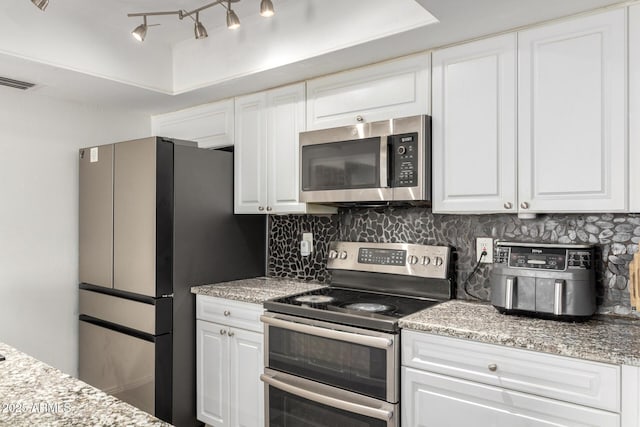 kitchen with stainless steel appliances, visible vents, white cabinetry, light stone countertops, and tasteful backsplash