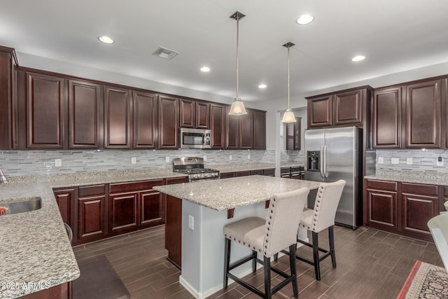 kitchen featuring stainless steel appliances, backsplash, a sink, a kitchen island, and dark brown cabinets