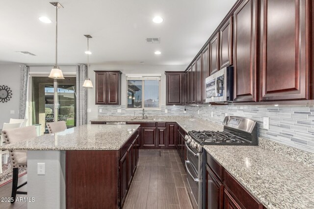 kitchen featuring stainless steel appliances, a sink, tasteful backsplash, light stone counters, and a breakfast bar area