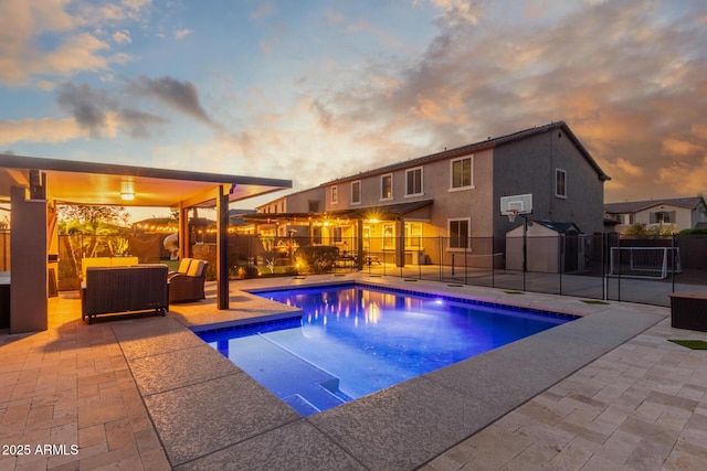 pool at dusk with a patio area, fence, and an outdoor living space