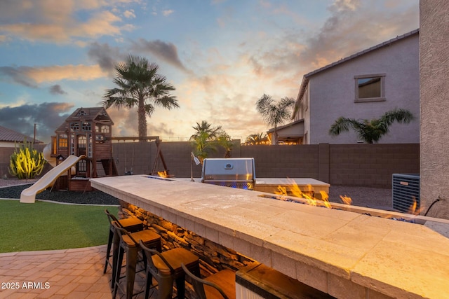 patio terrace at dusk featuring a grill, central AC unit, and a playground