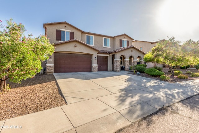 mediterranean / spanish house with stucco siding, concrete driveway, stone siding, a tiled roof, and a garage