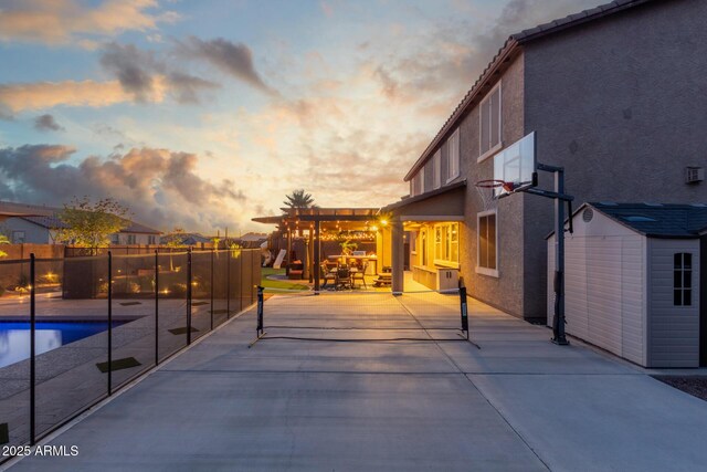 patio terrace at dusk featuring an outbuilding, a storage shed, fence, and cooling unit
