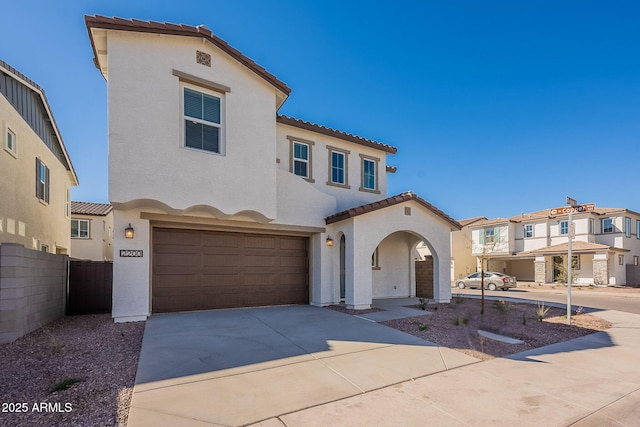 mediterranean / spanish-style home featuring stucco siding, a tiled roof, fence, a garage, and driveway
