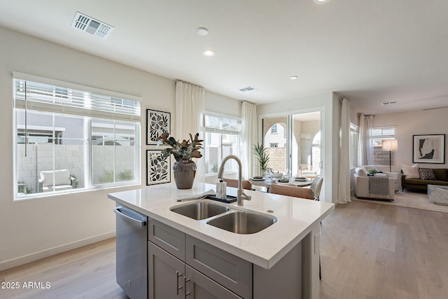 kitchen with a sink, dishwasher, light wood-style flooring, open floor plan, and light stone countertops