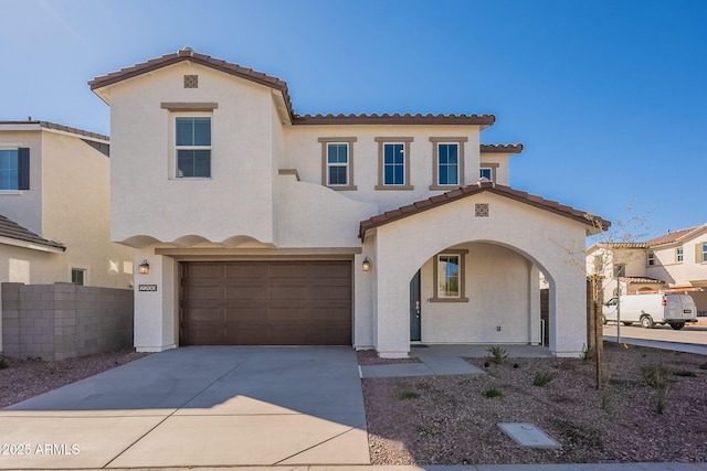 mediterranean / spanish house with a tiled roof, stucco siding, an attached garage, driveway, and fence