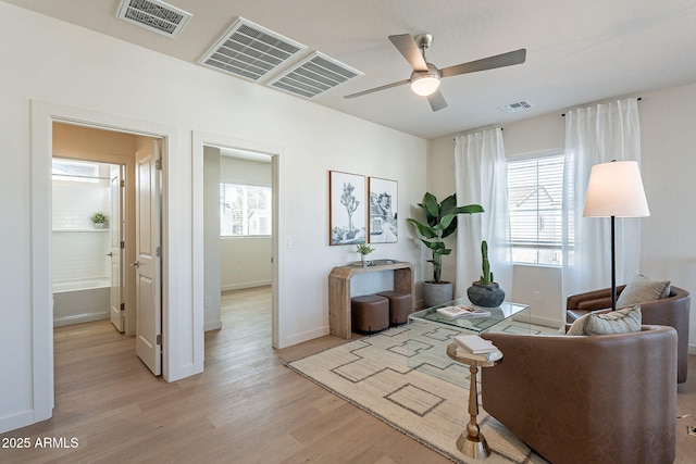 living area with light wood-style floors, a ceiling fan, and baseboards