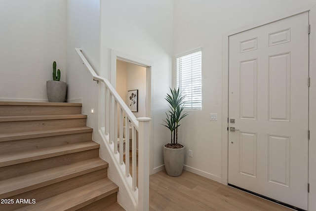 foyer entrance with light wood-type flooring, stairs, and baseboards