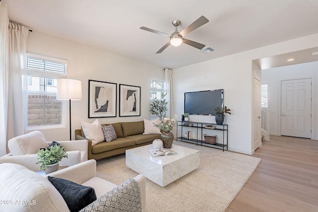 living room with light wood-type flooring, plenty of natural light, a ceiling fan, and baseboards