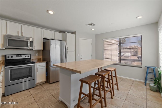 1703 E Palo Blanco Way, Gilbert, AZ 85296 - kitchen with stainless steel appliances, light tile patterned floors, white cabinets, a kitchen bar, and recessed lighting