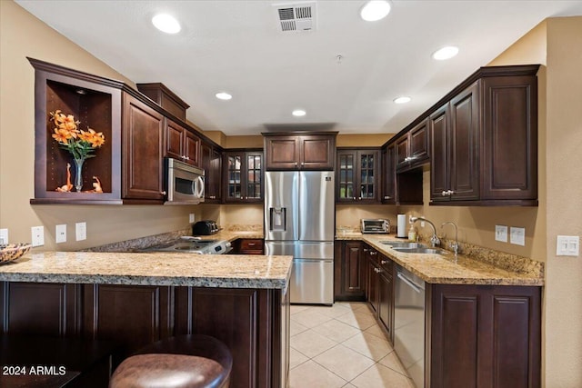 kitchen with kitchen peninsula, appliances with stainless steel finishes, a kitchen bar, dark brown cabinetry, and sink