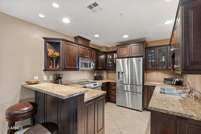 kitchen featuring kitchen peninsula, a kitchen bar, light stone countertops, stainless steel appliances, and sink