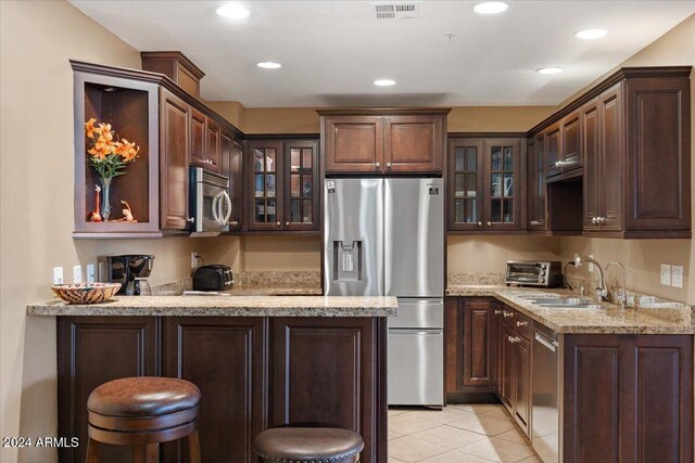 kitchen with a breakfast bar, light stone countertops, light tile patterned floors, dark brown cabinets, and stainless steel appliances