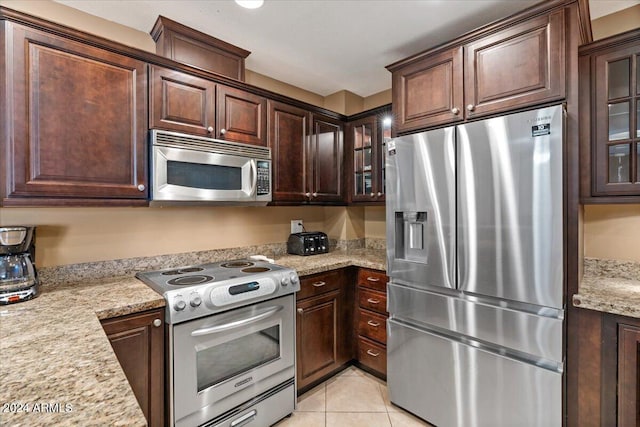 kitchen with dark brown cabinets, light tile patterned flooring, light stone countertops, and stainless steel appliances