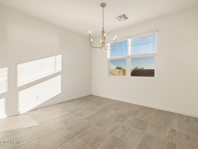 tiled spare room with a chandelier