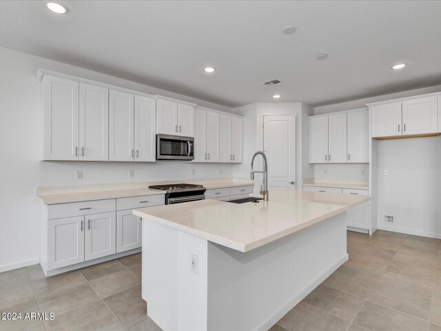 kitchen with white cabinetry, sink, a center island with sink, light tile patterned flooring, and appliances with stainless steel finishes