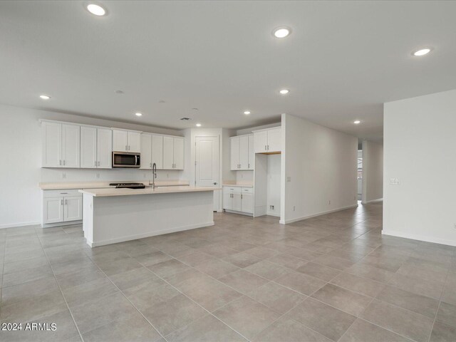 kitchen featuring white cabinets, light tile patterned floors, and a kitchen island with sink