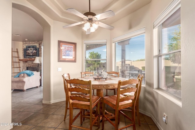 tiled dining space featuring ceiling fan, a healthy amount of sunlight, and a fireplace