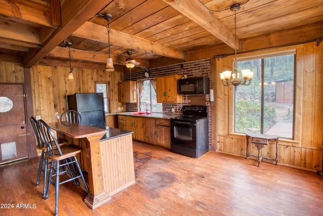 kitchen with a sink, wood walls, hanging light fixtures, and black appliances