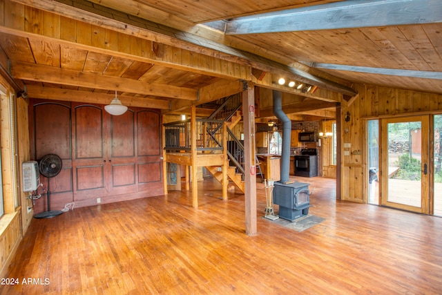 unfurnished living room featuring wooden ceiling, vaulted ceiling with beams, a wood stove, light hardwood / wood-style flooring, and wood walls