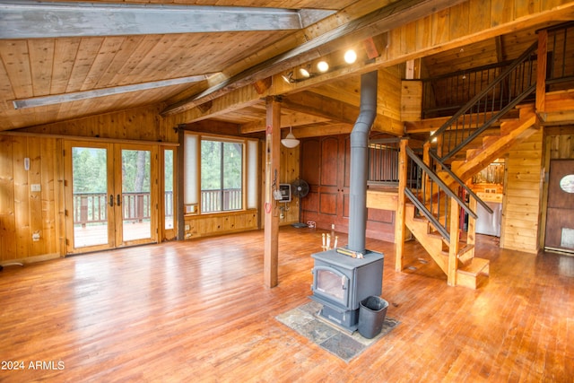 living area with lofted ceiling with beams, a wood stove, wooden walls, light wood-type flooring, and wooden ceiling