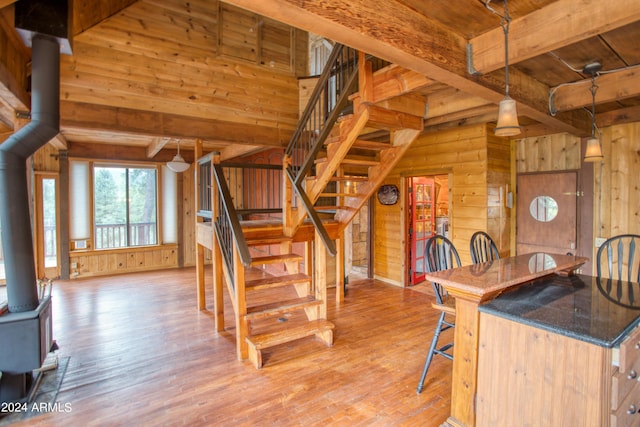 interior space featuring light wood-type flooring, a wood stove, wooden walls, and beam ceiling