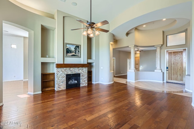 unfurnished living room featuring a high ceiling, wood-type flooring, ornate columns, and a fireplace